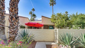A courtyard with a pathway, palm trees, and a building with a red umbrella. - Condo w/ Patios & Community Pools in Palm Springs! (Palm Springs)