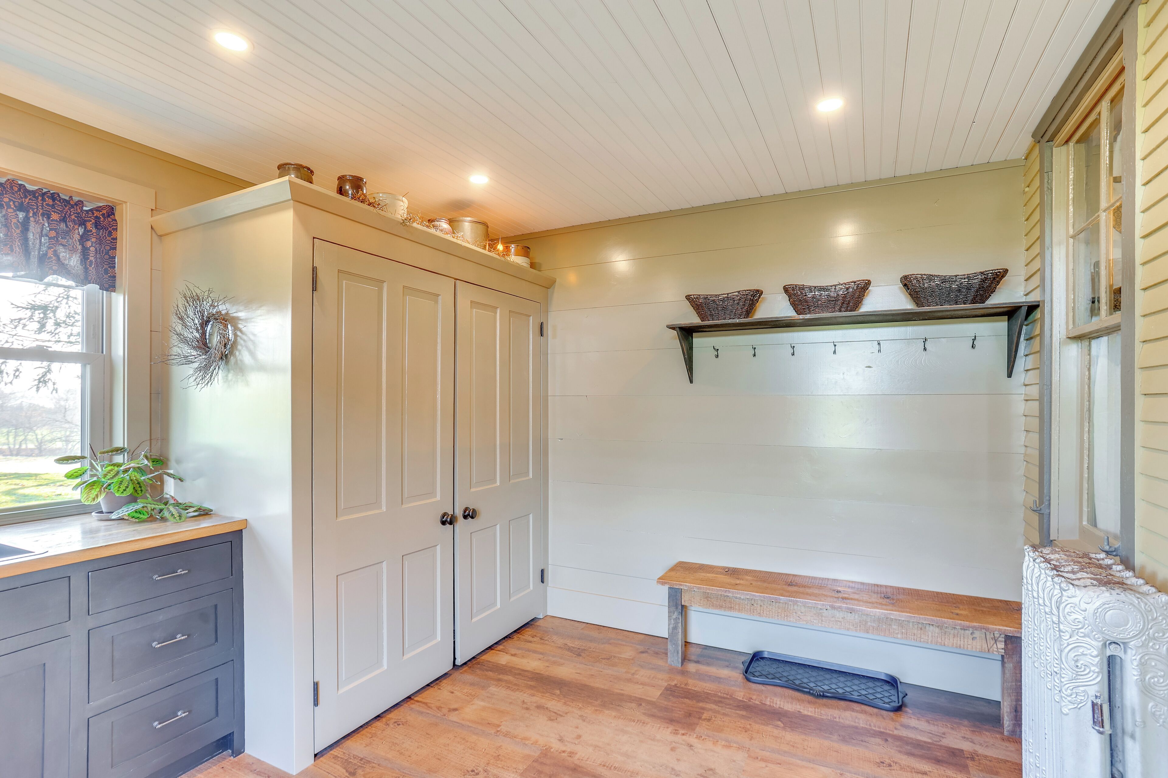 A kitchen with a wooden bench, white cabinets, and a window with a view.