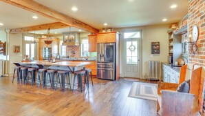 A spacious kitchen with a large island, wooden bar stools, and a brick accent wall. - 3 Mi to Dtwn: Charming Farmhouse in Mount Joy! (Mount Joy)