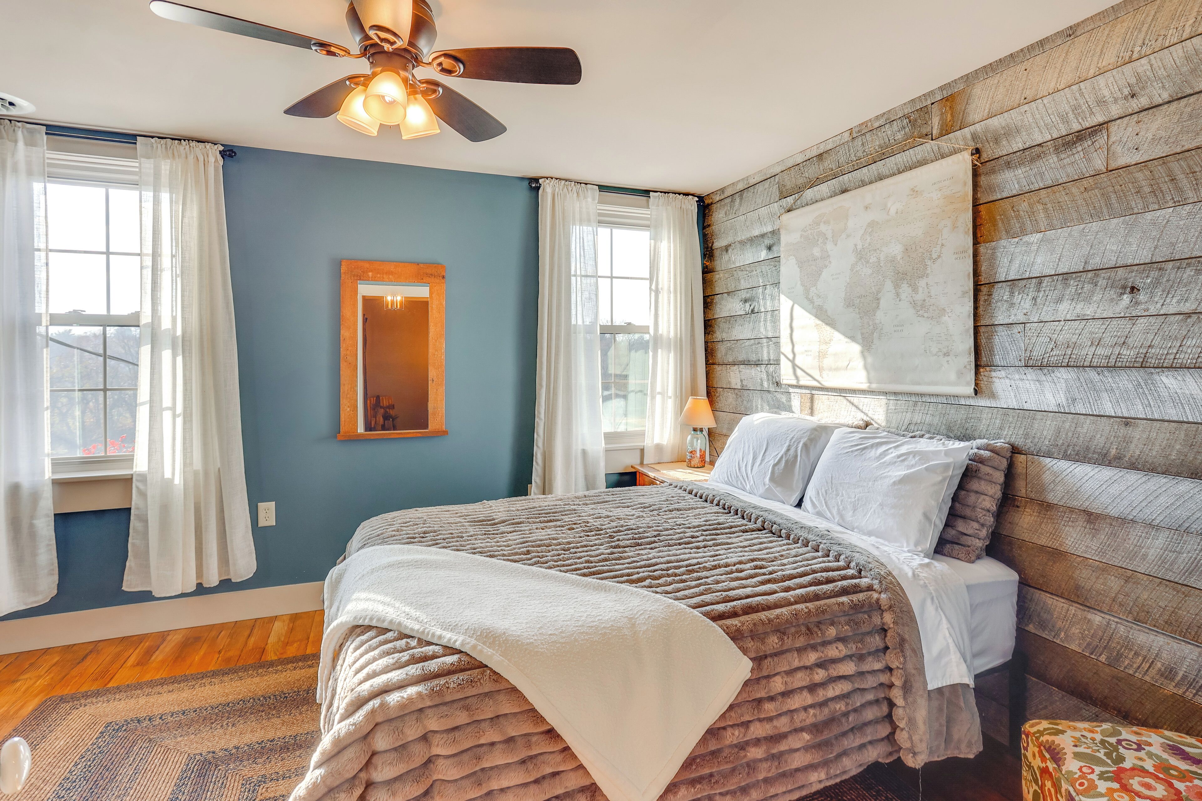 A bedroom with a bed, a ceiling fan, a world map on the wall, and a window with curtains.