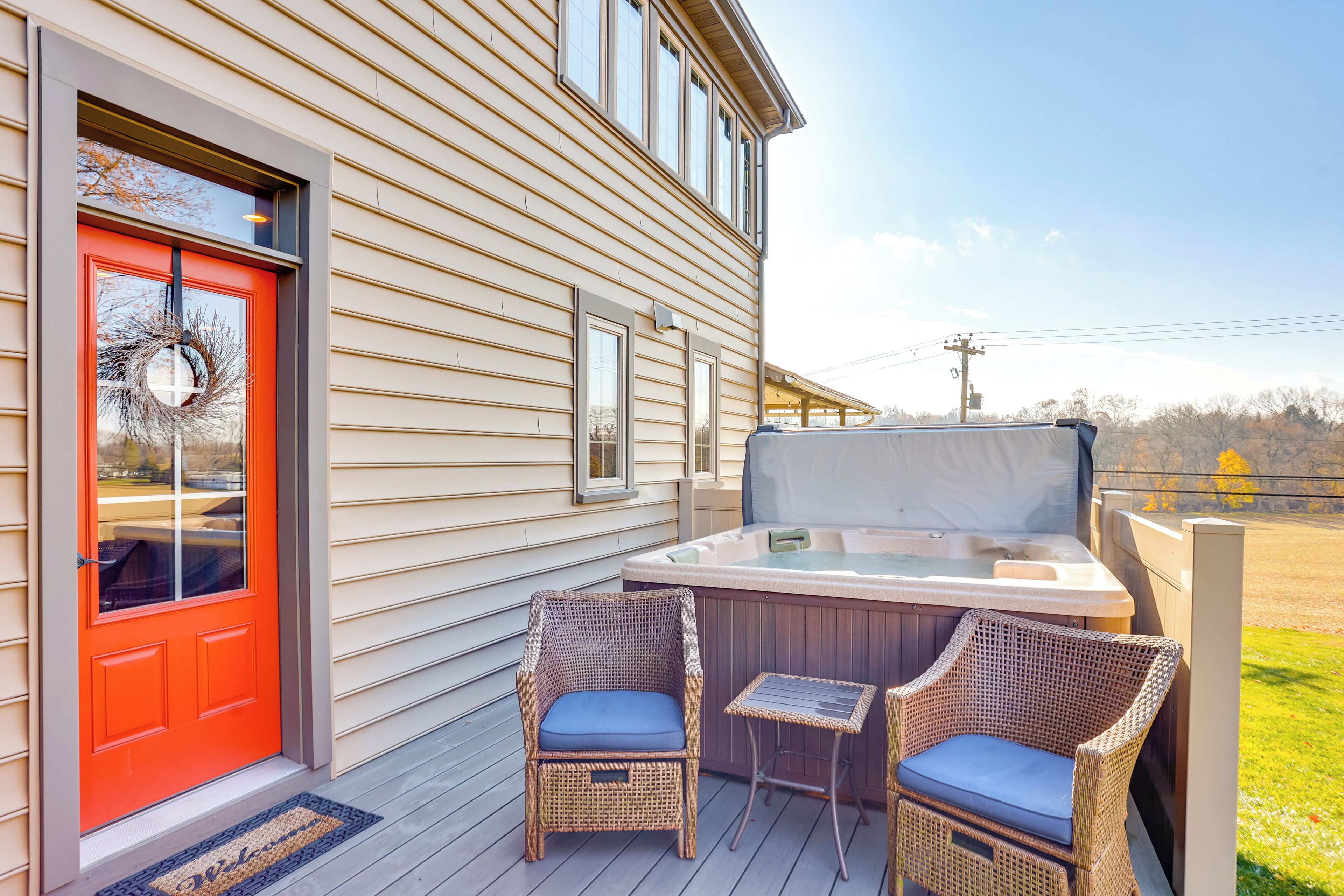 A house with a red door, a hot tub, and two wicker chairs with blue cushions on a wooden deck.