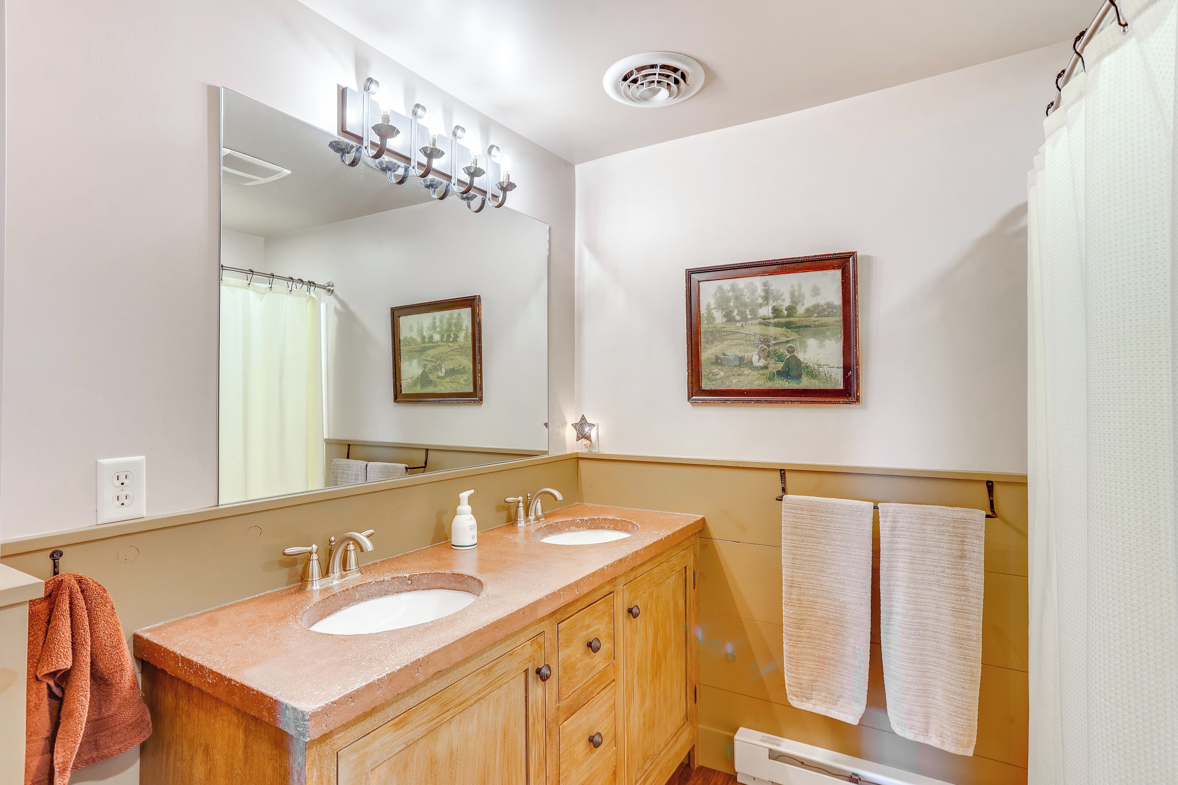 Une salle de bain avec deux lavabos, un miroir, un rideau de douche et un tableau encadré au mur.
