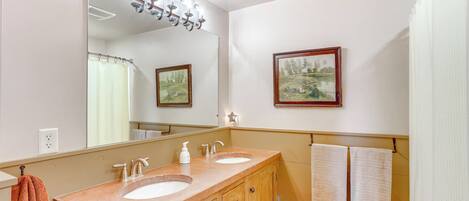 Une salle de bain avec deux lavabos, un miroir, un rideau de douche et un tableau encadré au mur.