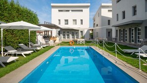 A swimming pool with lounge chairs and umbrellas, surrounded by modern buildings and a well-maintained lawn. - Aristi House in Olimpiada (Aristotelis)