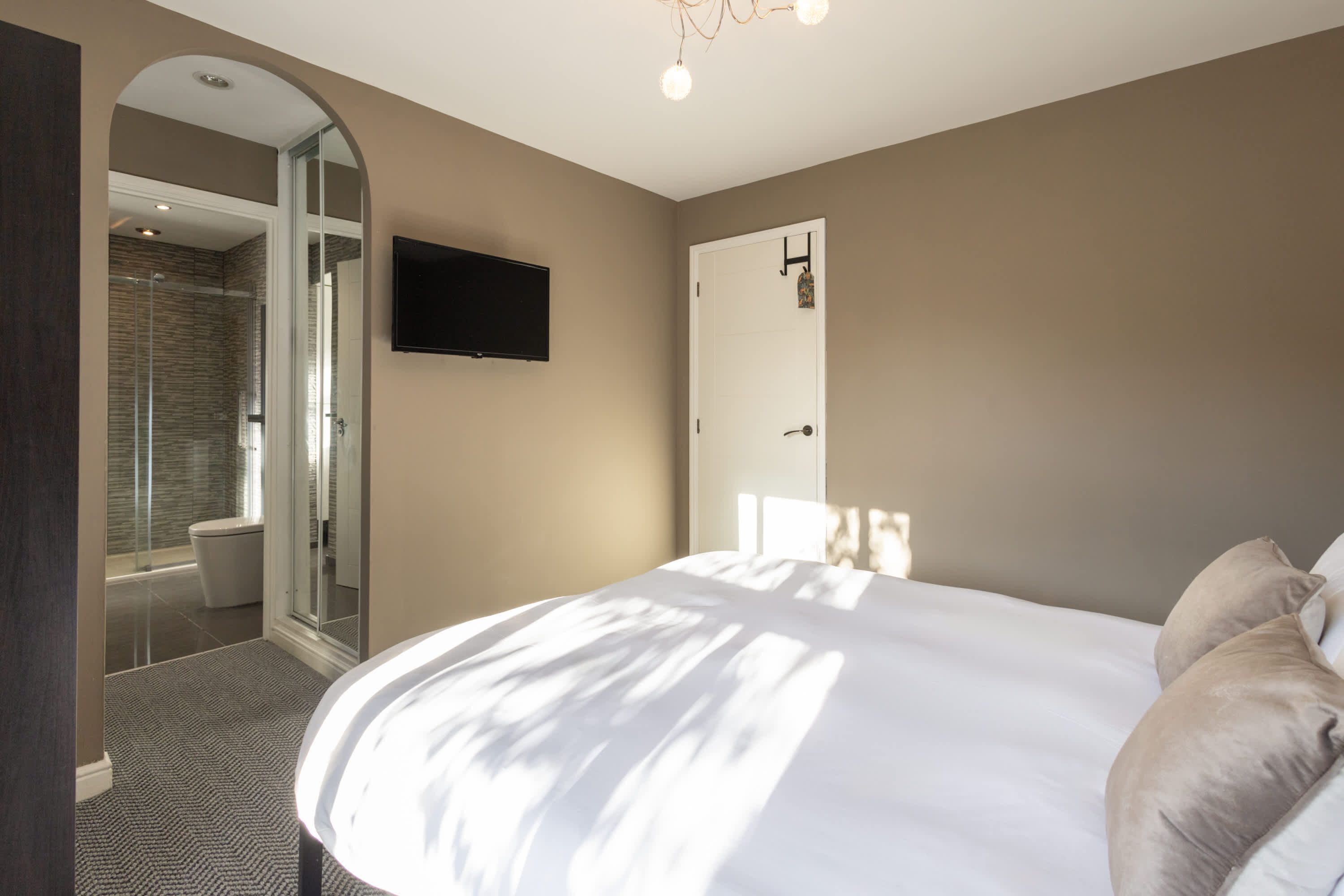 A bedroom with a large bed, a TV mounted on the wall, and a door leading to a bathroom.