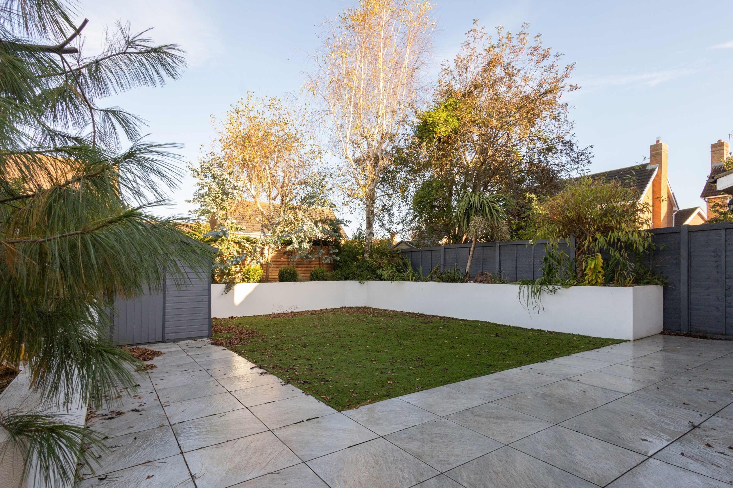 A backyard with a lawn, a white planter box, and a grey fence.