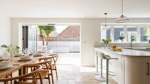 Une cuisine moderne avec des meubles blancs, un grand îlot central doté de tabourets de bar et un coin repas avec des chaises en bois et une table en verre.