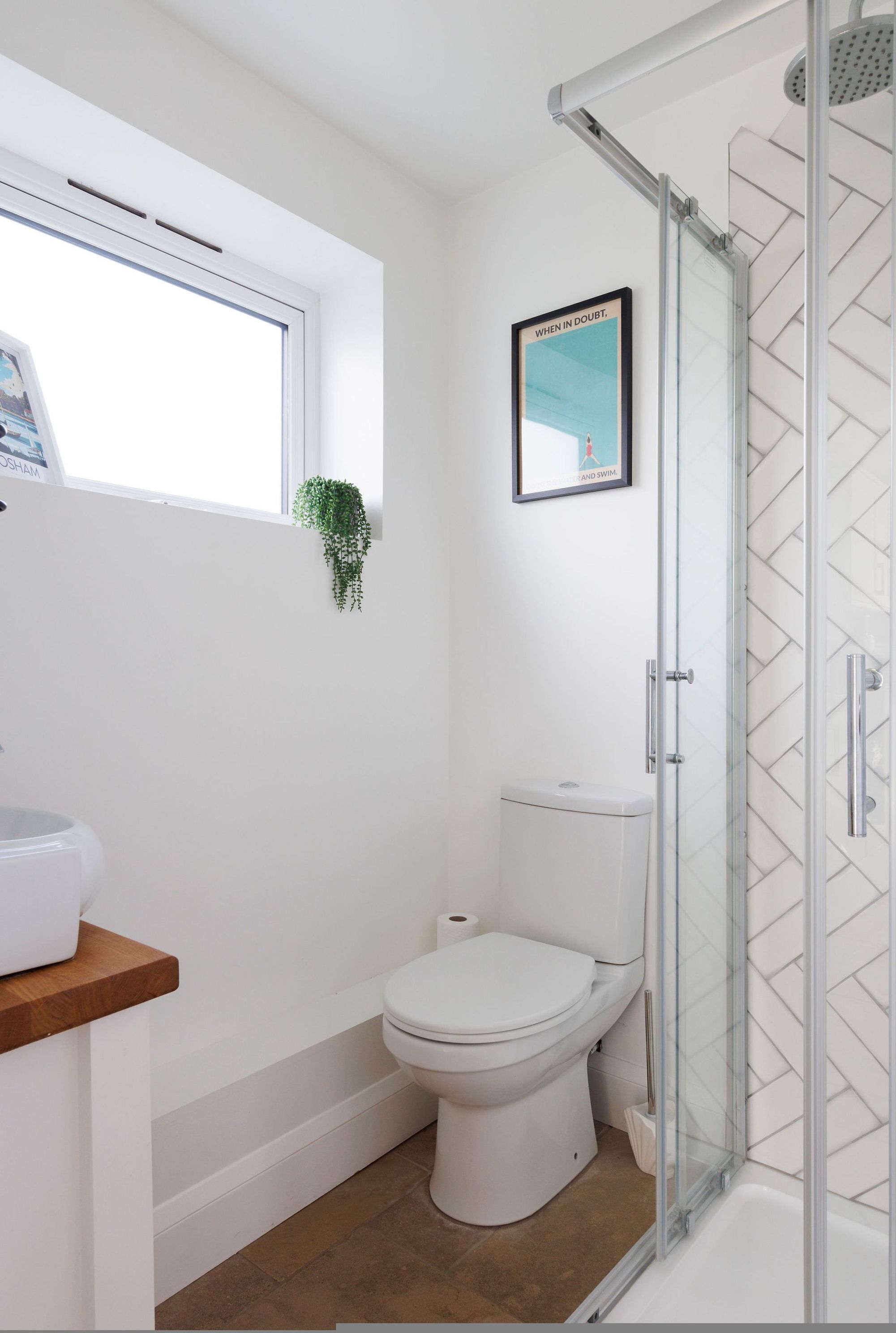 Ein modernes Badezimmer mit Toilette, Dusche und einem Fenster mit Pflanze.