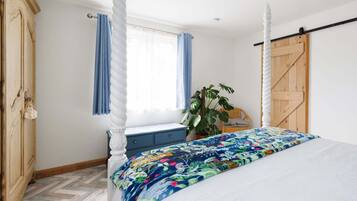 A bedroom with a four-poster bed, a wooden wardrobe, a window with blue curtains, and a potted plant.