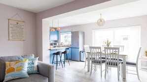 A modern kitchen with blue cabinets, a dining area with white chairs, and a grey sofa with decorative pillows.