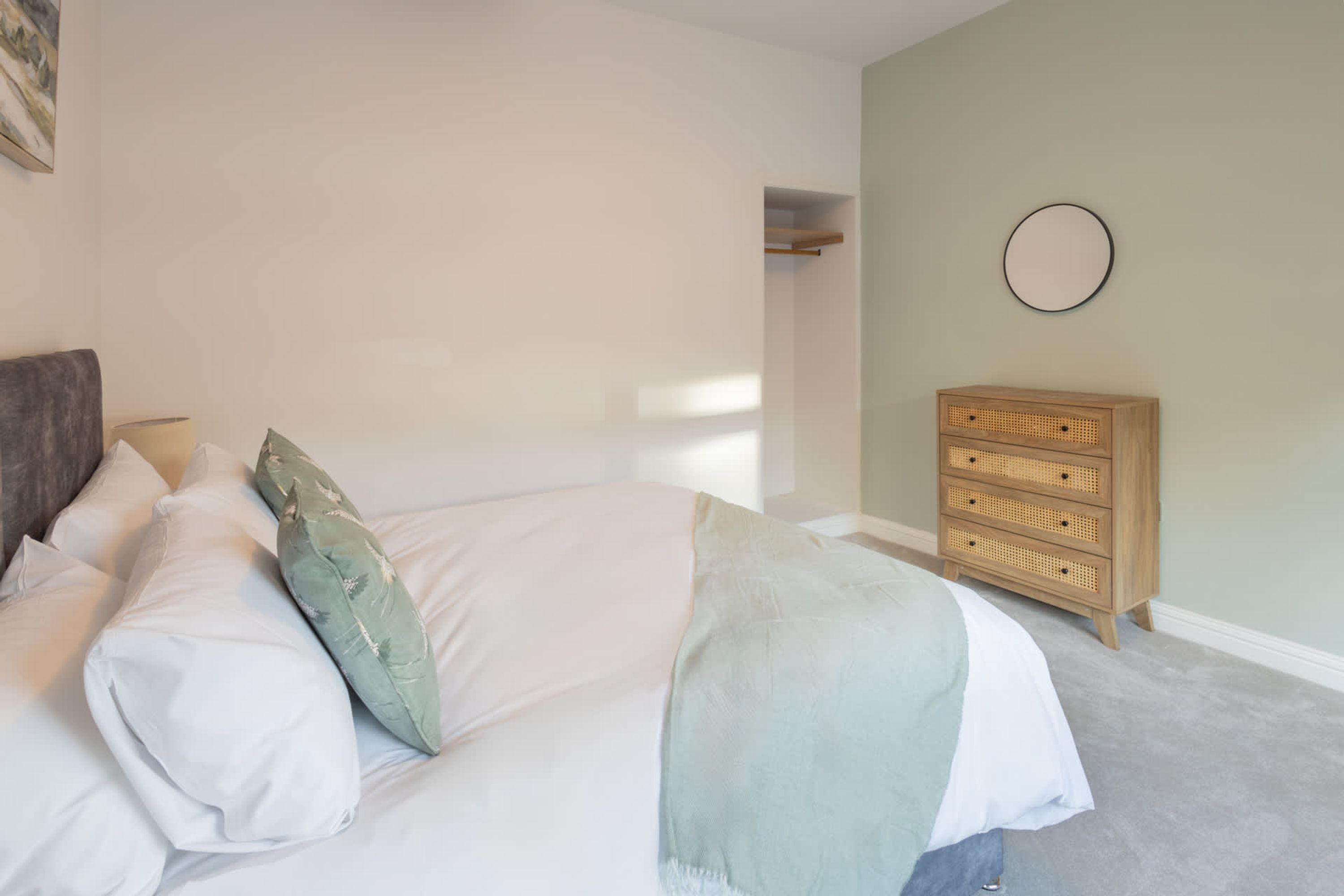A bedroom with a bed, pillows, a dresser, and a wall-mounted mirror.