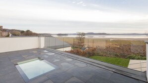Una terrazza panoramica sul tetto con una zona vetrata, una piscina e vista su un fiume e colline lontane.