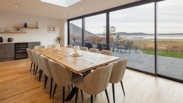 Zona pranzo moderna con un ampio tavolo in legno, sedute confortevoli e vista all'esterno attraverso ampie finestre.