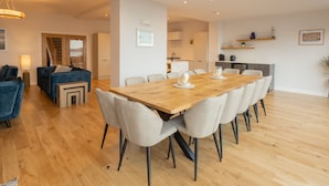 Un'area living moderna con un tavolo da pranzo in legno, sedie di colore chiaro, un divano e una zona cucina.