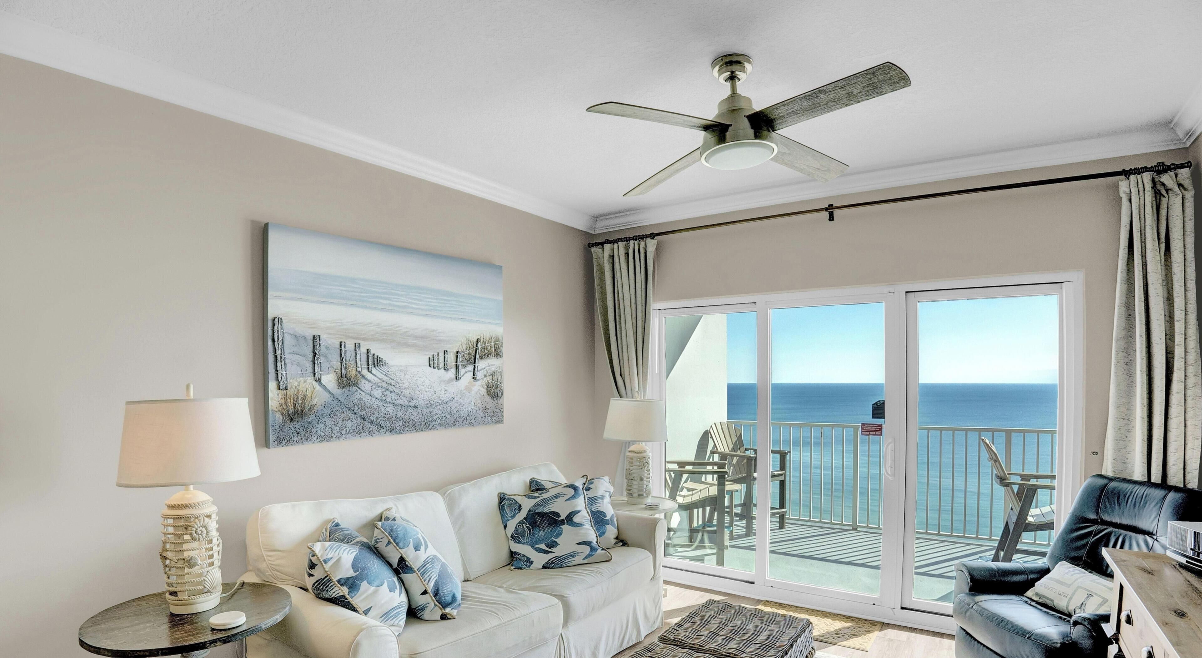 Ein Wohnzimmer mit einer Couch, einem Couchtisch, einer Lampe und einem Gemälde. Ein Balkon bietet Blick auf den Ozean.