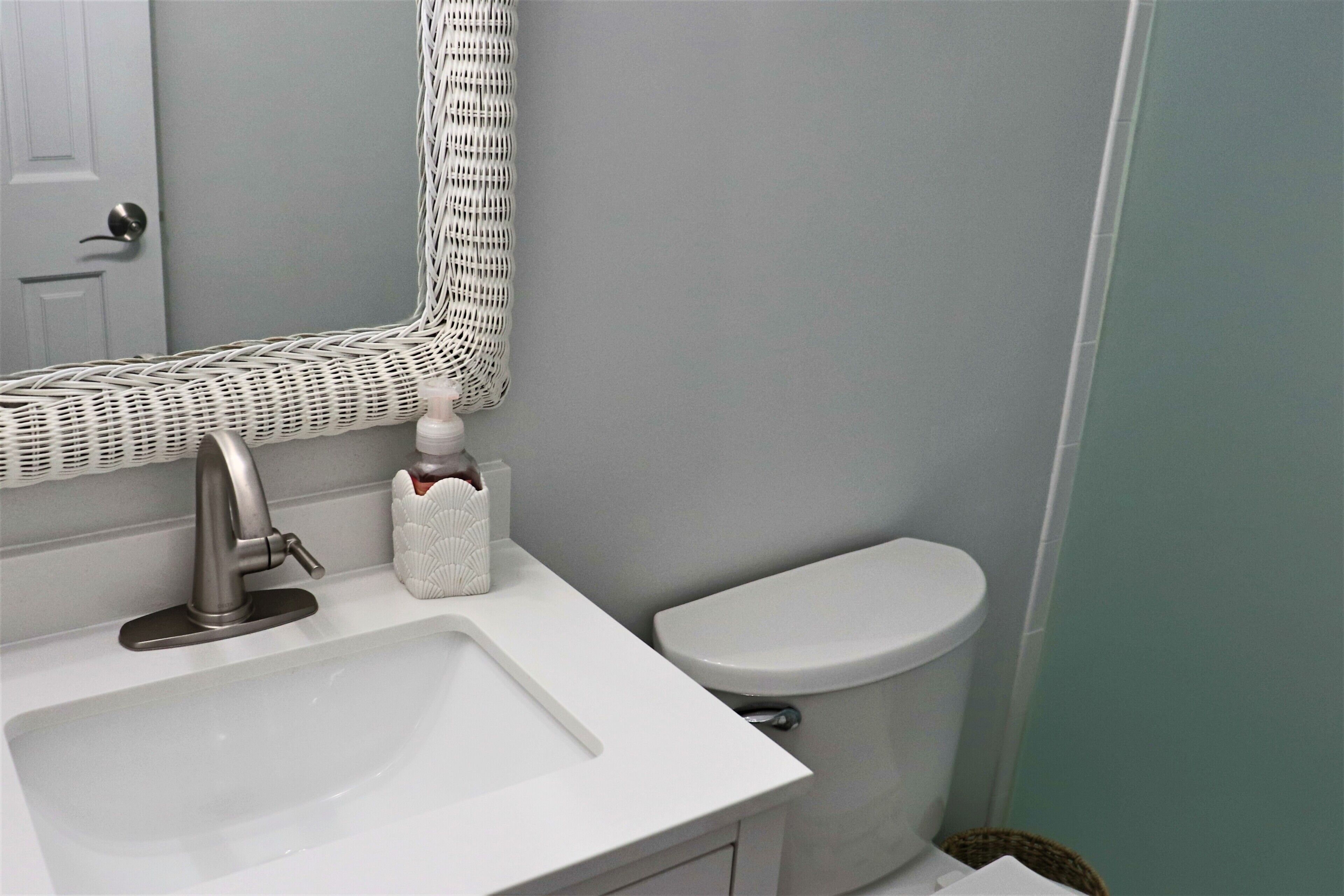 Et badeværelse med en hvid vask, toilet og et spejl med en fletramme.