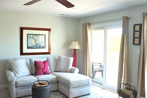 A living room with a sectional sofa, a lamp, a framed picture, a sliding glass door, and a small table with a basket.