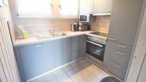 Eine kompakte Küche mit grauen Schränken, einer Spüle, einer Mikrowelle, einer Kaffeemaschine und einem Backofen.