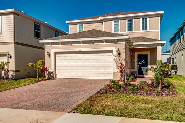 A two-story house with a garage, a brick driveway, and small landscaped garden with various plants. - 16235 Luxury Retreat Your Perfect Getaway Family Home (Clermont)