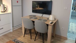 Une cuisine compacte équipée d’un réfrigérateur, d’une machine à café et d’un téléviseur fixé au mur.