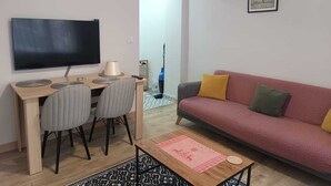 Un salon comprenant un téléviseur, un canapé, une table basse et un coin repas avec des chaises.