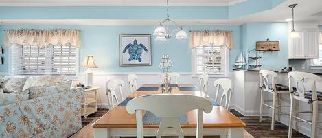 A dining area with a wooden table and white chairs, a blue wall, and a ceiling light.