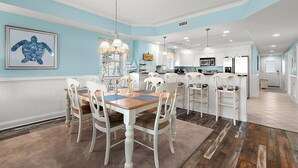 A spacious kitchen with white cabinetry, a central island, and a dining area with a wooden table and white chairs.