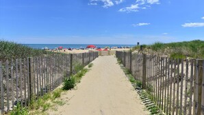 A sandy pathway leading to a beach with a wooden fence on either side.