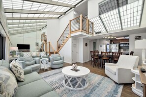 A spacious living area with a high ceiling, a staircase, and a kitchen.