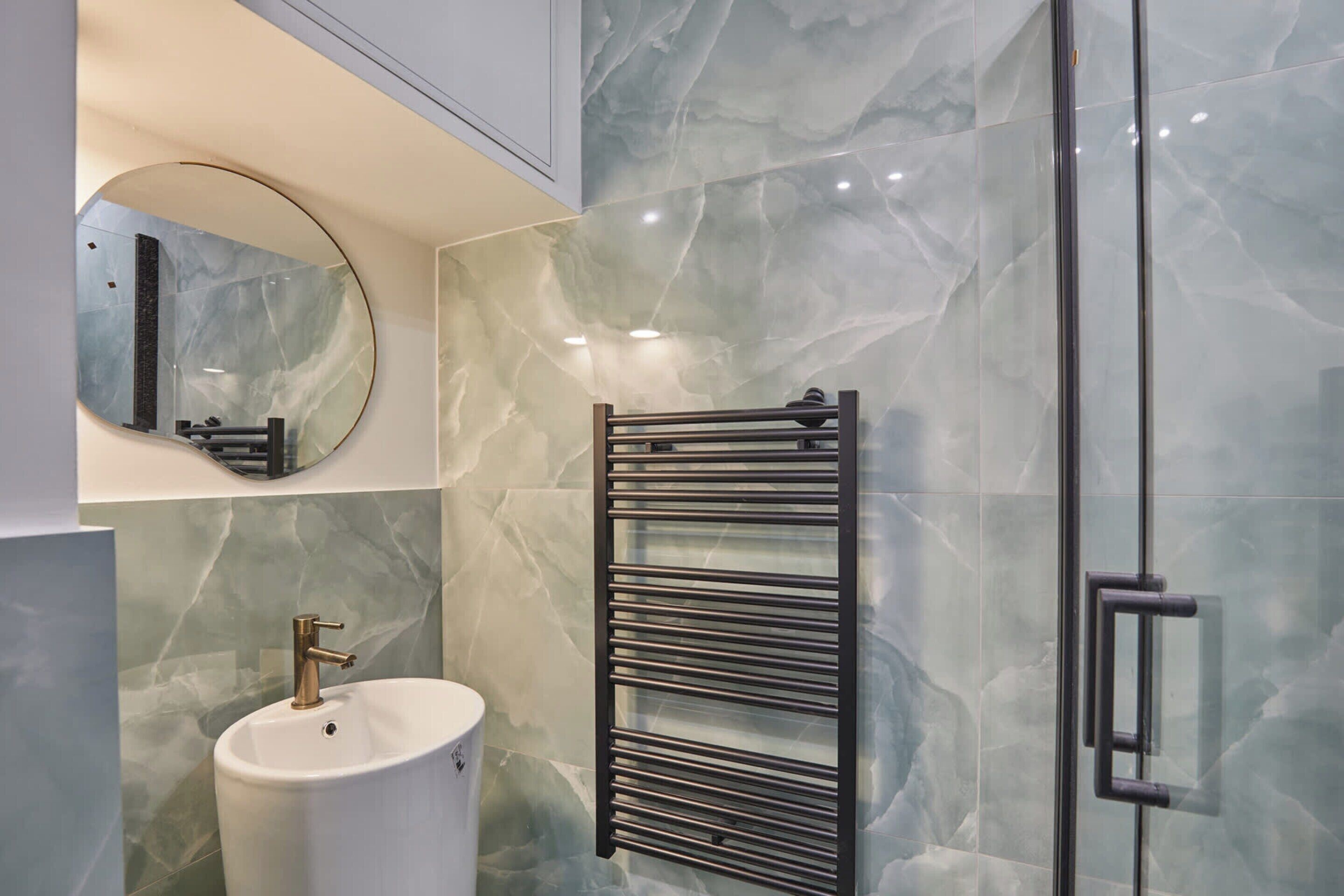 A modern bathroom with a white sink, a round mirror, and a glass shower enclosure.