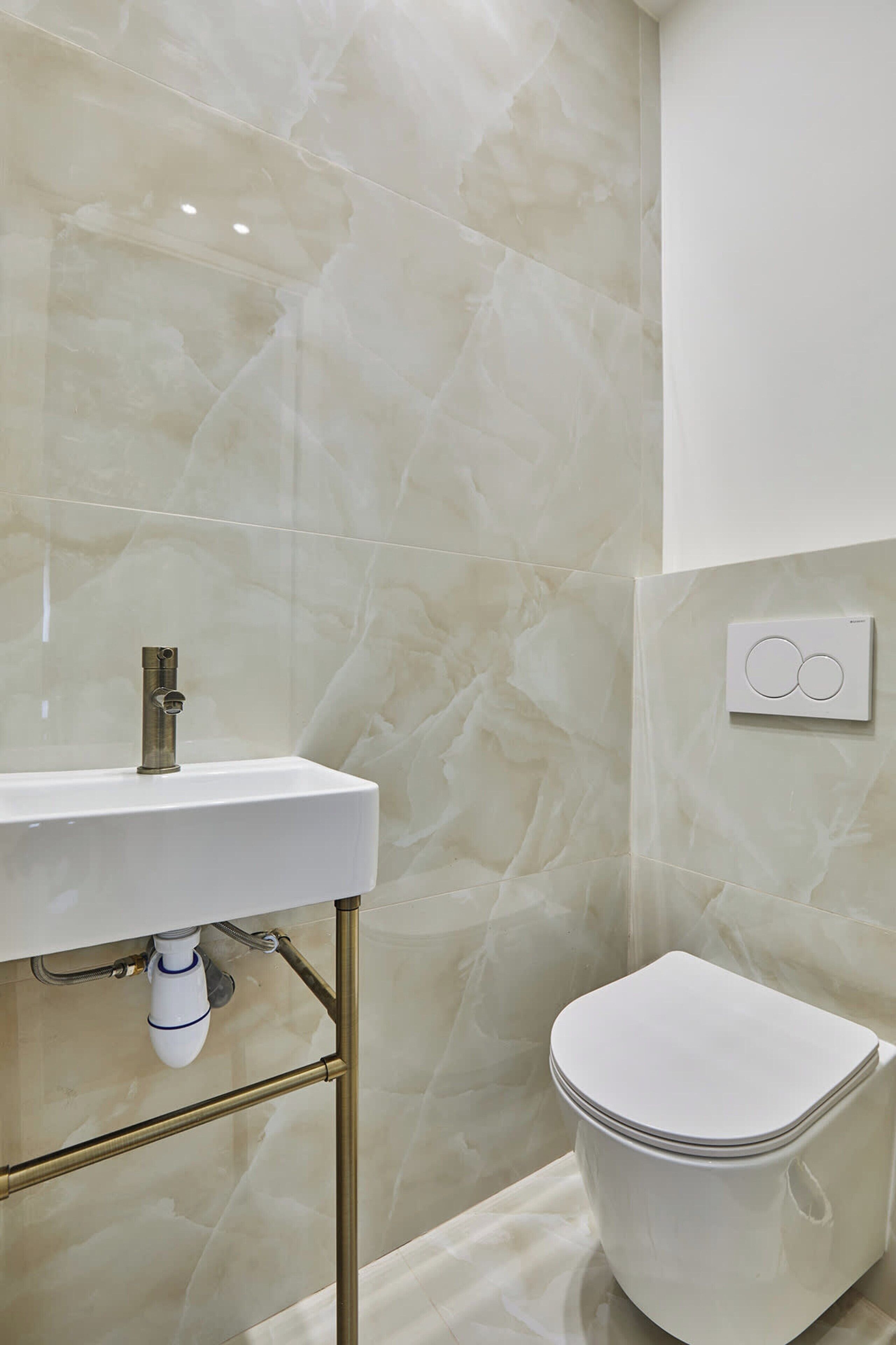 A bathroom with a white sink, gold fixtures, and a toilet.