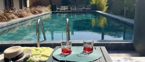 Zona junto a la piscina con una mesa, sillones reclinables y una pileta.
