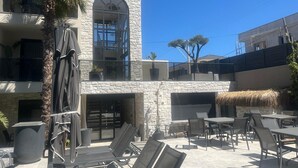 Un patio con asientos al aire libre, un edificio de piedra con un amplio ventanal arqueado y una palmera.
