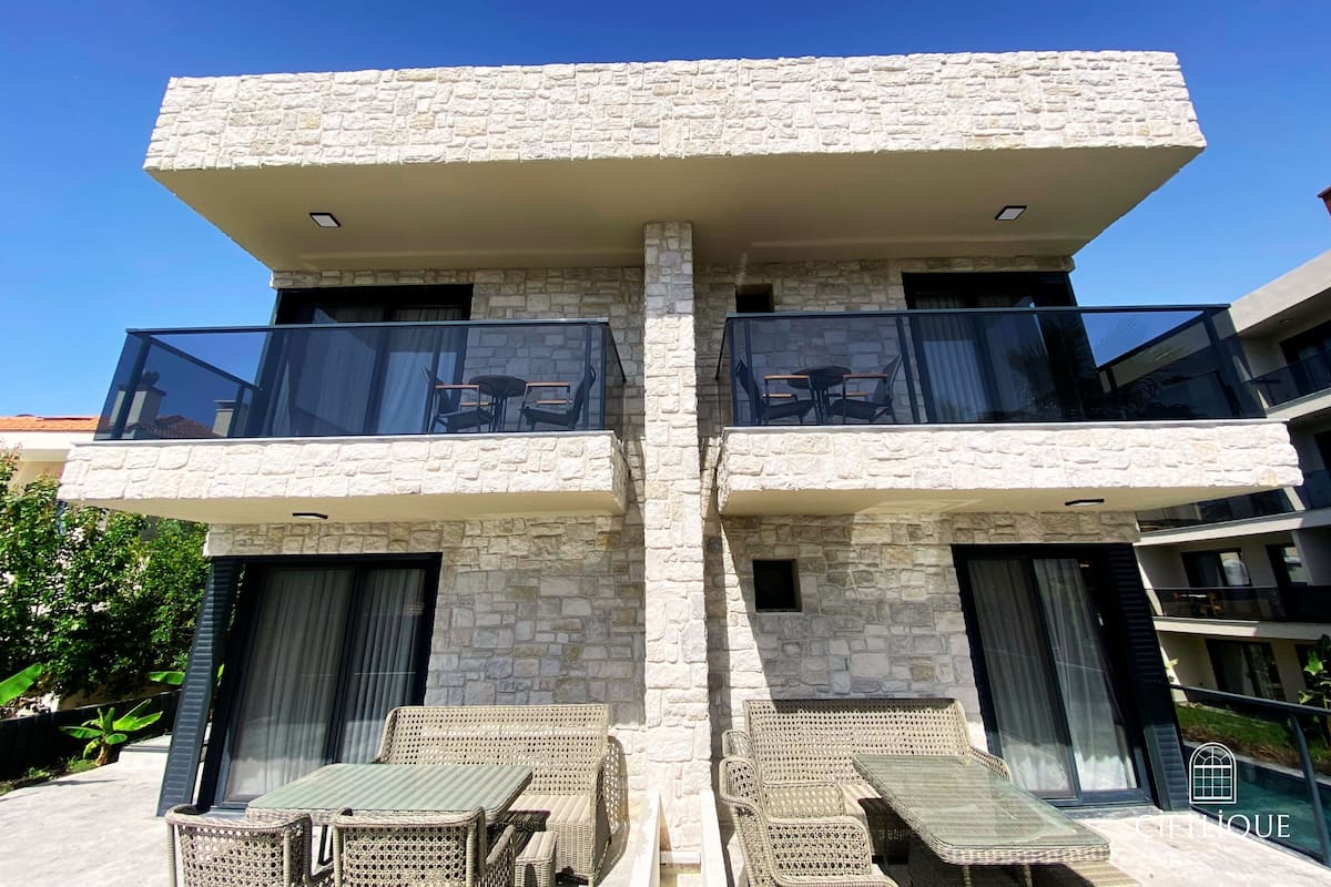 Un edificio moderno con dos balcones, cada uno con barandilla de vidrio y mobiliario exterior.
