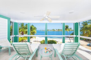 A room with a view of the ocean, two chairs, a table, and a ceiling fan.