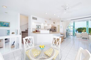 A modern kitchen with white cabinetry, a central island, and a dining area with wicker furniture.