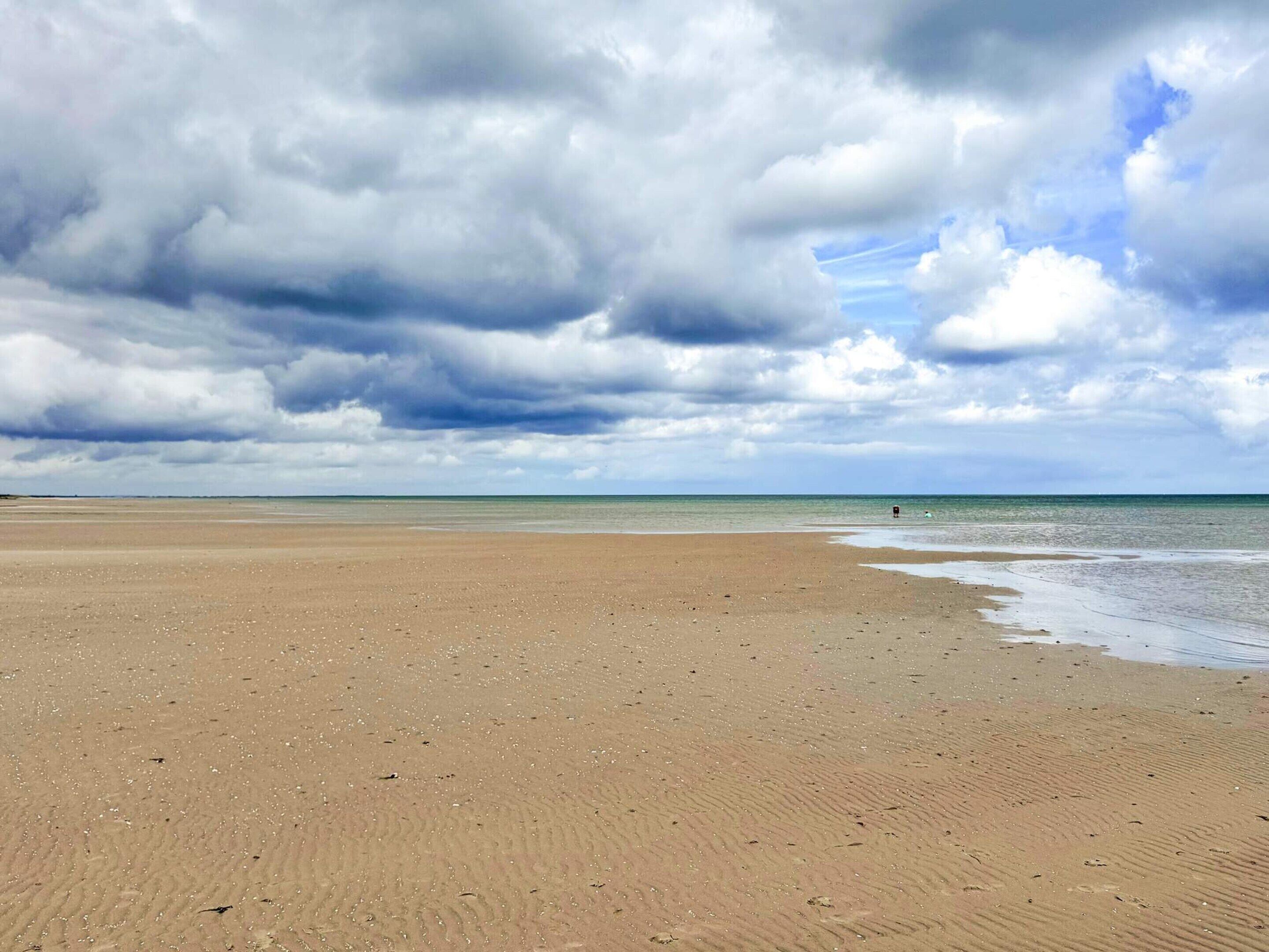 A wide sandy beach with a calm sea under a cloudy sky.