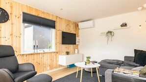 A modern living room with a wooden wall, a flat-screen TV, a round coffee table, and a grey sofa.