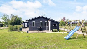 A black house with a patio, a swing set, and a slide in the yard.