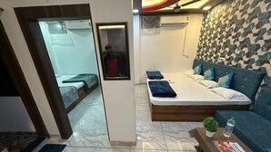 Een moderne hotelkamer met een bed, een bank, een klein tafeltje met een plant en een waterfles, en een kamer met een patroon op de muur.