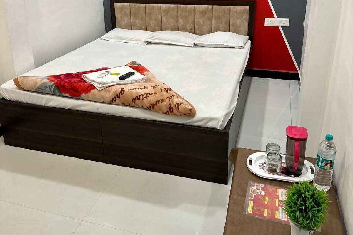 A modern bedroom with a bed, a nightstand, a red and grey accent wall, and a small potted plant.