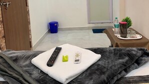 Hotelkamer met een bed, een aan de muur bevestigde televisie, een airconditioningapparaat, een deur en een klein tafeltje met een plant en waterflessen.