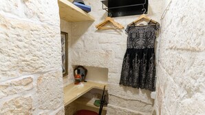 A small, stone-walled room with a wooden desk, a red chair, and a black lace dress hanging on the wall.