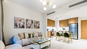 Ein modernes Wohnzimmer mit einem Glastisch, einer Couch und einem Essbereich mit Stühlen und einem Tisch. Es gibt eine Küchenzeile mit Holzschränken und einem Kühlschrank.