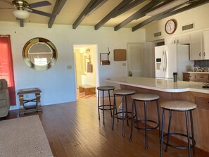 Une cuisine moderne avec un plan de travail blanc, des tabourets de bar et une horloge au mur.