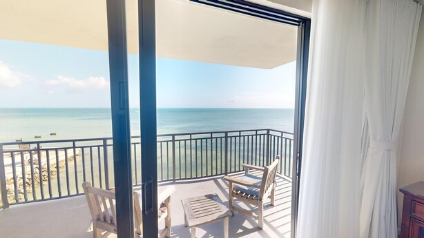 Een balkon met uitzicht op zee, een houten stoel, een klein tafeltje en een witte gordijn.