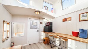 Una cocina compacta con encimera de madera, dos taburetes tipo bar, un refrigerador y un microondas.