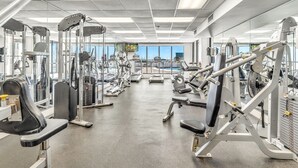 A gym with various exercise machines, large windows, and a view of the city.