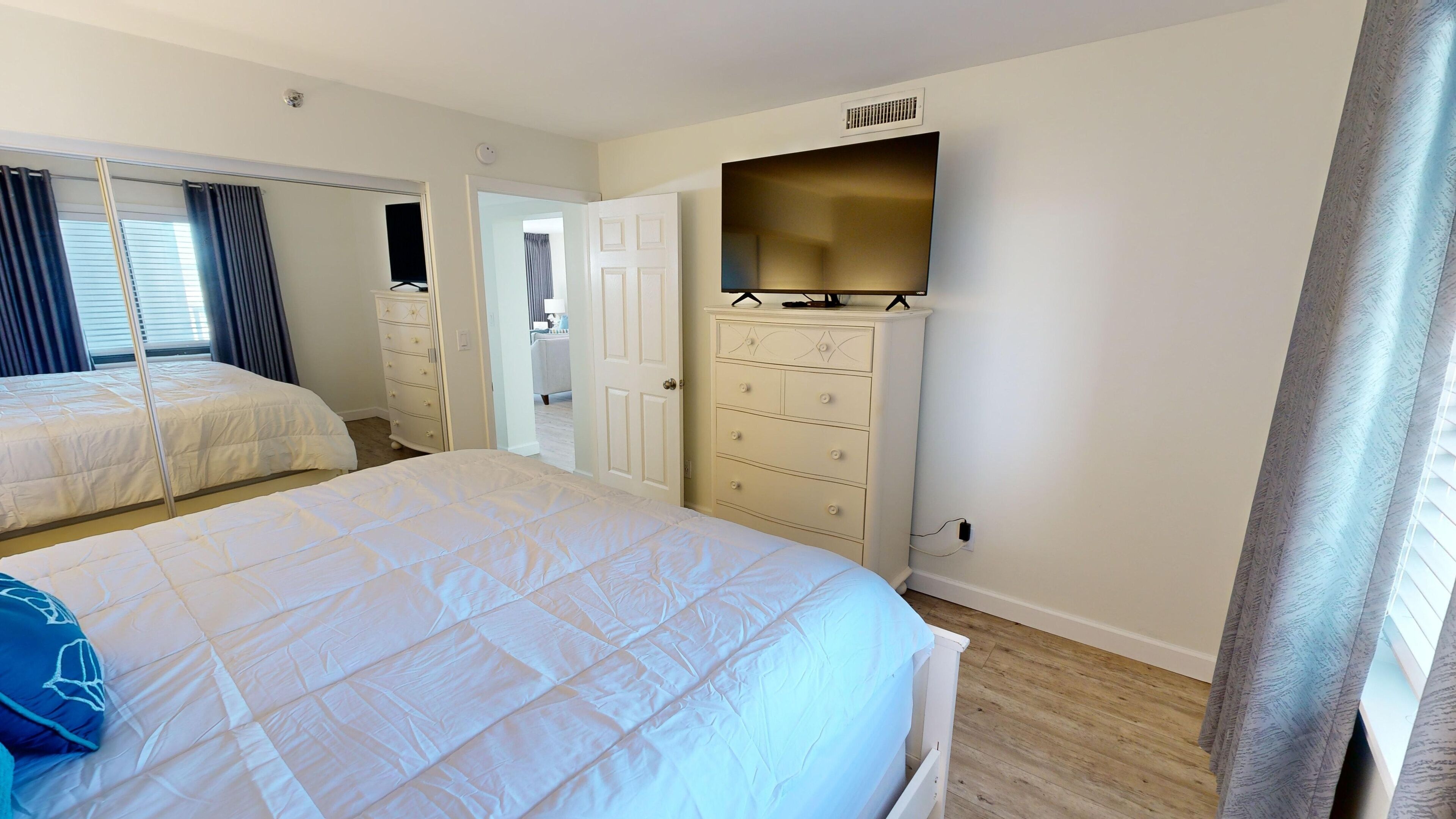 A bedroom with two beds, a dresser, and a television on a stand.