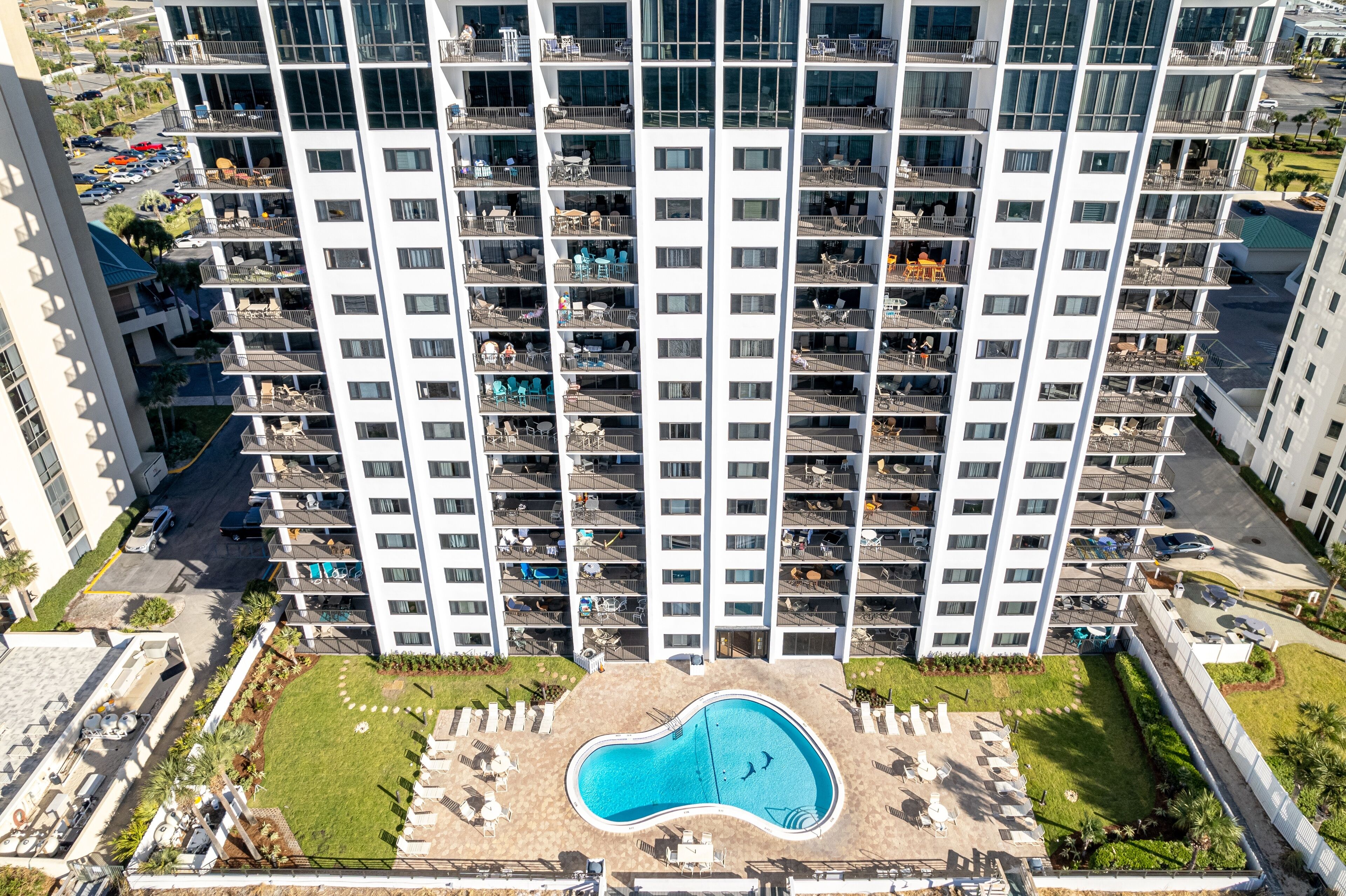 A high-rise building with multiple balconies, a swimming pool, and a parking area.